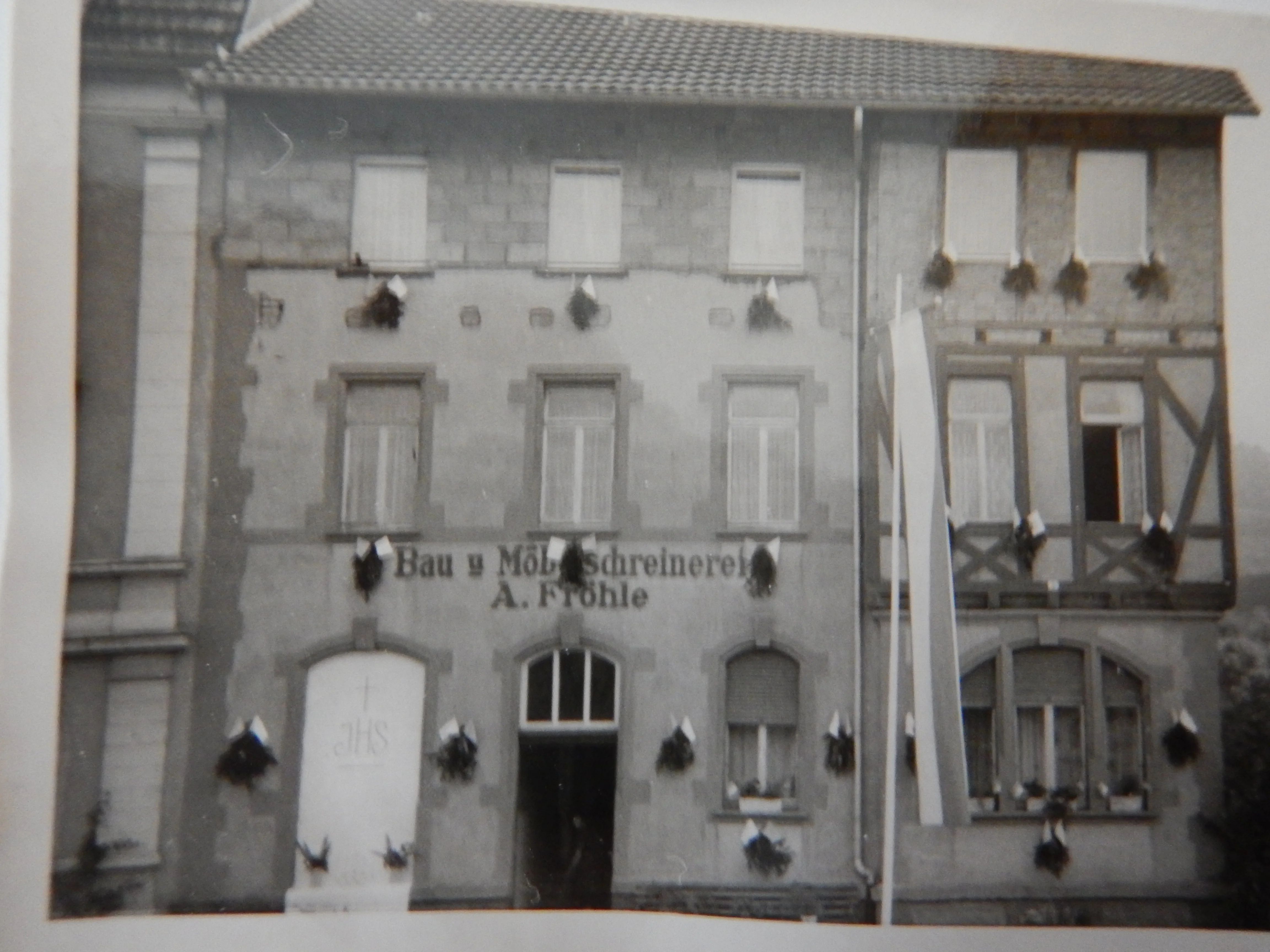 Historische Aufnahme des Wohnhauses mit Schreinerei und dekorativem Trauerschmuck an der Fassade